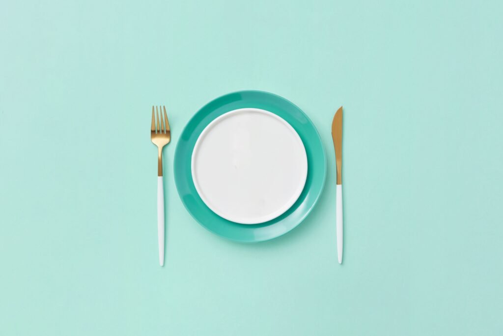 Minimalist plate with fork and knife on teal background