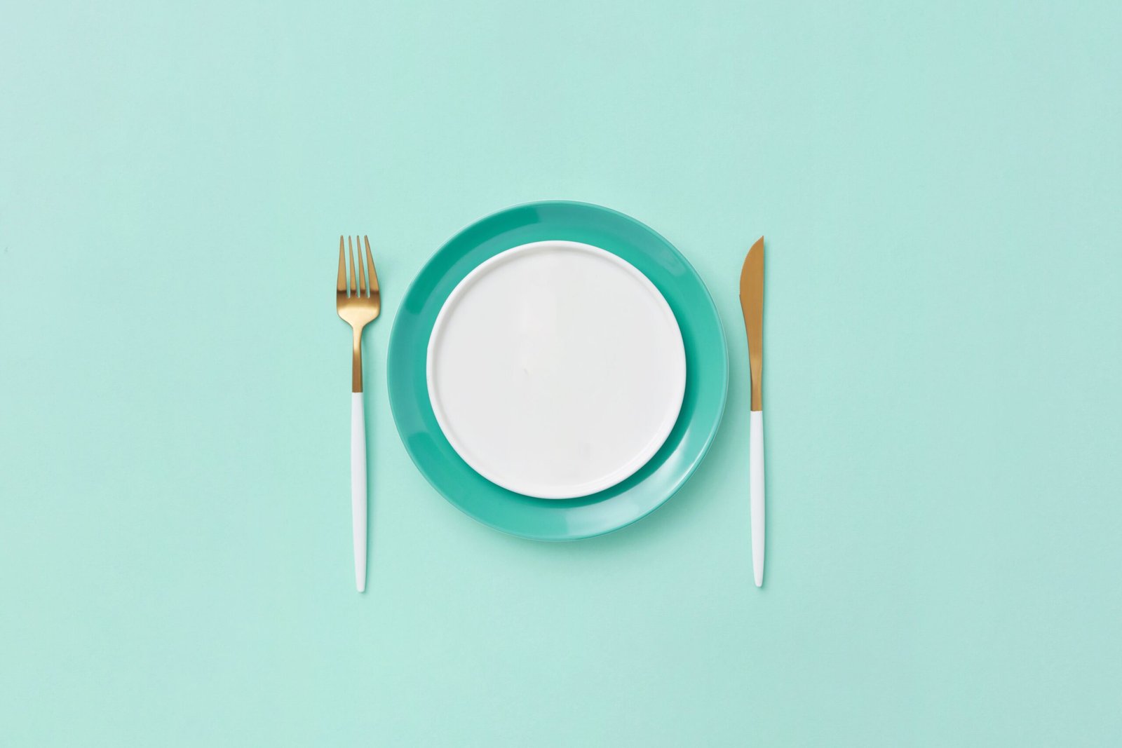 Minimalist plate with fork and knife on teal background